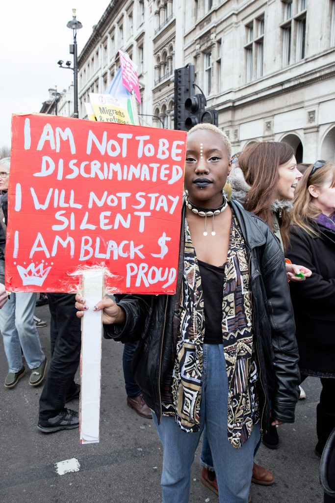 An anti-racism protester holding a sign saying: I am not to be discriminated, I will not stay silent, I am black and proud. 