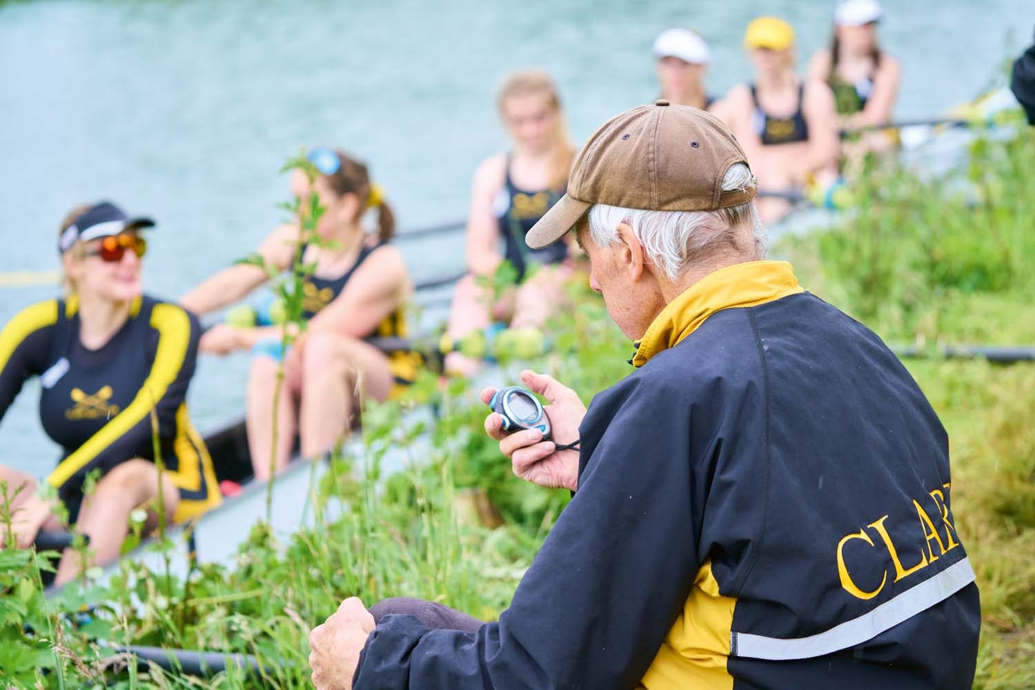 Coach on bank with stopwatch. Students in boat.