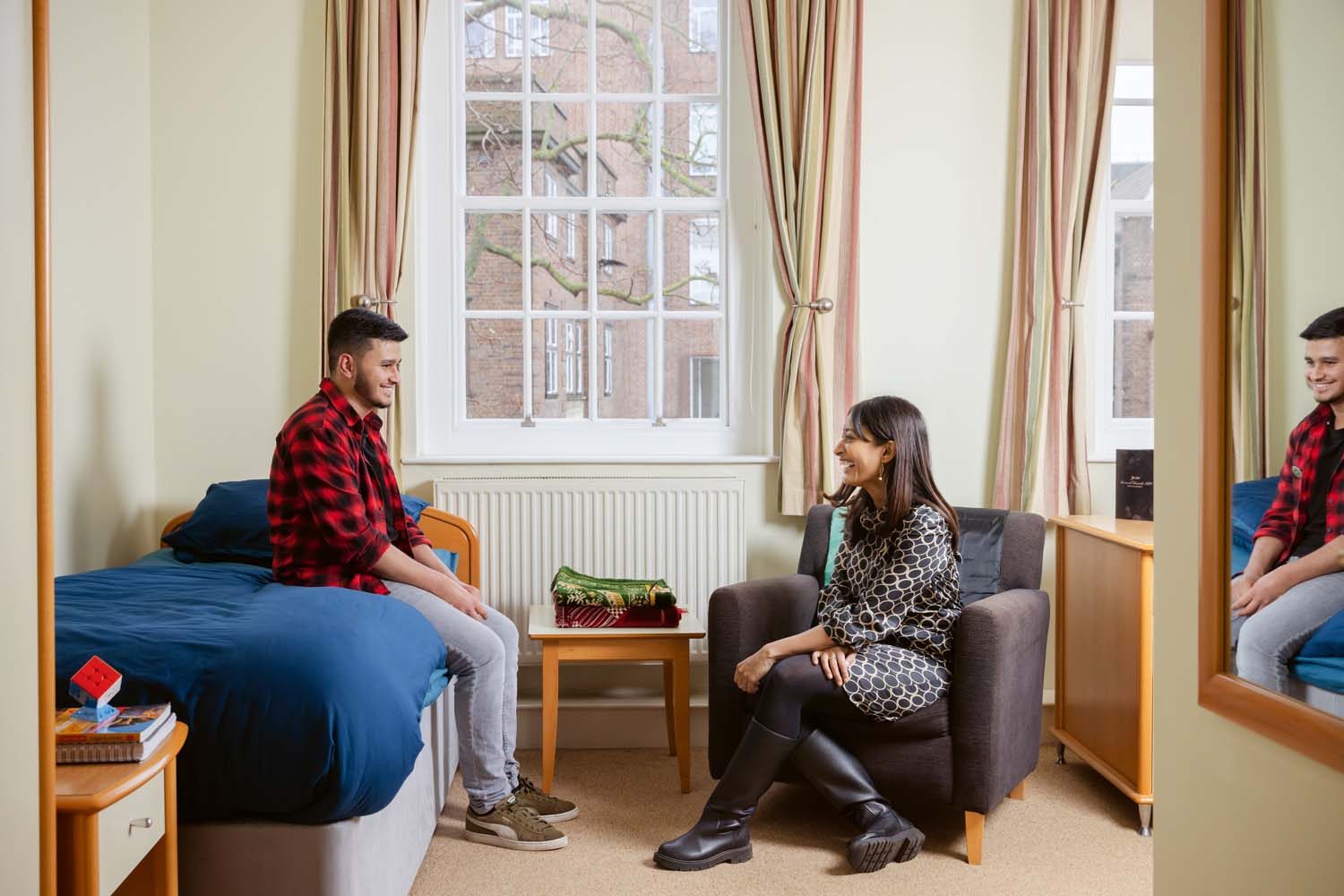 Dharshini David sits on chair chatting to Jiyaad Ali who sits on bed.